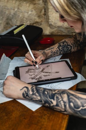 Photo for Vertical photo Close-up of a tattoo artist's hands as they fine-tune a design on a digital drawing pad, surrounded by sketches.Concept business, art. - Royalty Free Image