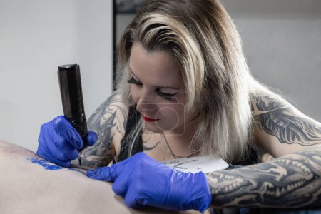 Photo verticale un gros plan d'un tatoueur gants main saisissant la machine à tatouer, prêt à créer un art permanent sur la peau. Concept business, art.
