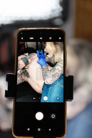 Fotografía vertical un primer plano de una pantalla de teléfono inteligente que muestra a un artista del tatuaje en el trabajo, centrándose en el arte y la habilidad involucrados. Copiar space.Concept negocio, arte.