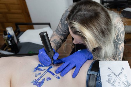 Foto horizontal Un atento artista del tatuaje trabaja en un tatuaje de escudo de armas, mostrando una mezcla de enfoque y habilidad delicada. Concepto negocio, arte.