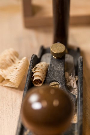 Vertical photo close-up view of a vintage hand plane in a woodworking workshop with fresh wood shavings curled atop the tool. Business concept.