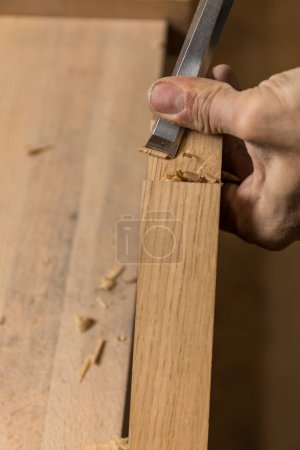 Vertical photo the photo focuses on a carpenter's precise hand movement while chiseling a notch in a wooden plank, with wood chips scattered around. Copy space. Business concept.