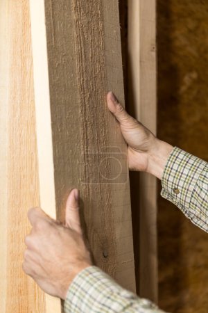 Vertikales Foto: Ein gelernter Schreiner inspiziert in einer Werkstatt die Qualität des Holzes, wobei seine Hände die Textur und Maserung für die Handarbeit beurteilen. Geschäftskonzept.