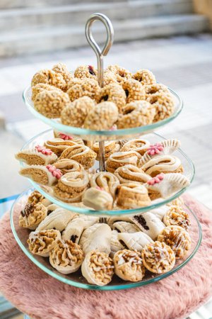 Vertical photo an inviting three-tiered stand overflows with an assortment of Arabic pastries, each variety offering a unique texture and taste, perfect for a festive gathering. Food and culture concept.