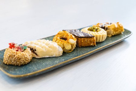 Foto horizontal una placa de cerámica azul alargada presenta maravillosamente una variedad de pasteles árabes gourmet, cada uno adornado con ingredientes y diseños intrincados. Concepto de alimentación y cultura.