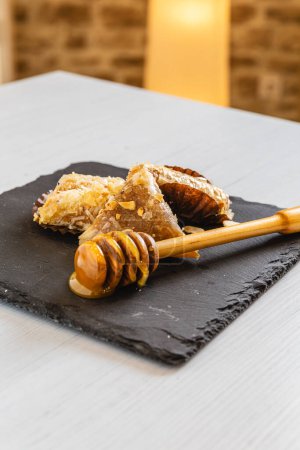 Foto vertical ricos y texturizados dulces árabes rociados con miel dorada, elegantemente puesta en escena en una superficie de pizarra áspera, encarnando encanto rústico y lujo culinario. Concepto de alimentación y cultura.