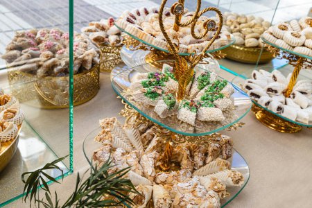 Horizontales Foto einer üppigen Präsentation arabischer Süßigkeiten mit einer Vielzahl von Texturen und Aromen, präsentiert auf exquisiten goldenen Ständern mit komplizierten Details. Ernährungs- und Kulturkonzept.