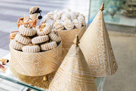 Horizontales Foto einer optisch ansprechenden Auswahl arabischer Süßigkeiten auf goldenen Ständern, mit kunstvollen geometrischen Stoffbezügen, die für kulturellen Reichtum sorgen. Ernährungs- und Kulturkonzept.