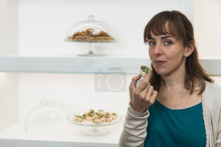 Horizontal photo a customer holds up a pistachio-covered dessert in a pastry shop, evaluating its appearance before taking a bite. Copy space. Food and culture concept.