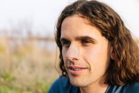 Horizontales Foto, ein Nahaufnahme-Porträt eines jungen Mannes mit langen, lockigen Haaren, der in die Ferne blickt. Lifestyle-Konzept.