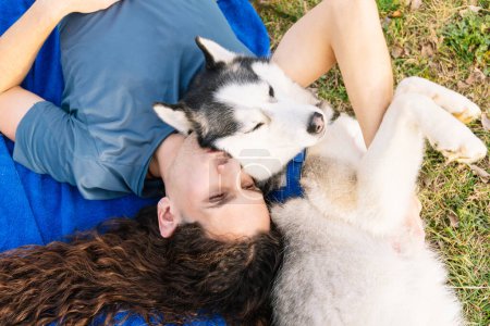 Horizontal photo in an endearing embrace, a man with curly hair and his husky share a tender moment, enjoying the warmth of each other's company on the grass. Lifestyle concept.