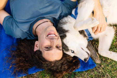 Horizontal photo a man and his husky playfully lie upside down on the grass, sharing a unique perspective and a joyful connection in the great outdoors. Lifestyle concept.