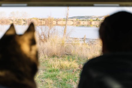 Horizontal photo inside a camper van, a husky and its owner enjoy a tranquil lakeside view, with the serene landscape spread out before them. Lifestyle concept.