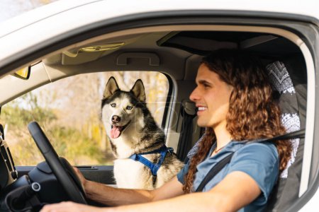 Horizontal photo a radiant man with long curly hair shares a driving moment with his excited Siberian Husky, both enjoying the sunny road trip in their camper van. Lifestyle concept.