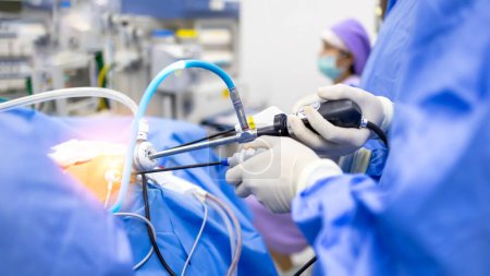 Doctor or Surgeon did laparoscopic or endoscopic minimal invasive surgery inside operating room in hospital.People hold medical instrument arthroscopic orthopedic surgery in blue uniform with light.