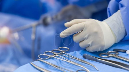 Photo for A surgeon or Doctor with nurse team in blue uniform did surgery inside operating room in hospital.Surgeon picking up surgical clamps and medical equipment with light.Emergency surgery was done. - Royalty Free Image