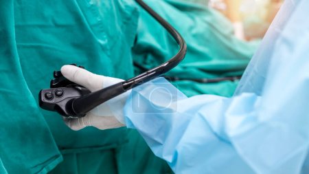 Ein Arzt oder Chirurg in einem hellblauen Schutzanzug führte eine Koloskopie oder Gastroskopie im Operationssaal des Krankenhauses durch. EGD-Technologie zur Krebsfrüherkennung. Grüner Hintergrund und Vordergrund verschwimmen..
