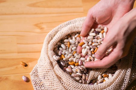 Mains ramassant divers haricots hérissés colorés d'un sac écologique rustique. Aliments entiers et alimentation saine dans un emballage durable.