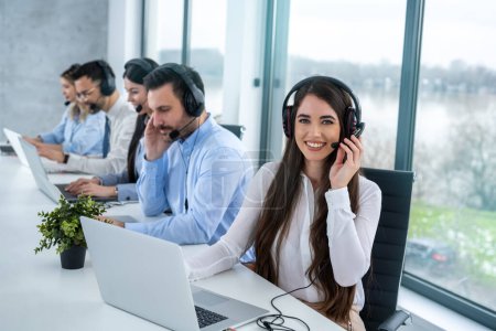 Photo for Call center agent woman with headset working on support hotline in modern office with group of customer support operators. - Royalty Free Image