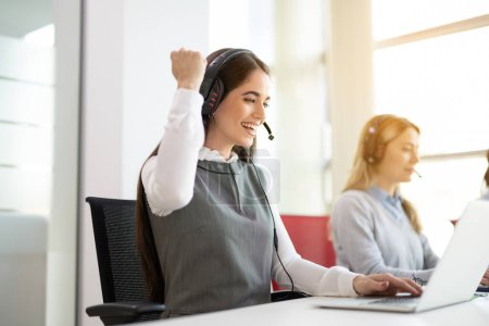 Operadora de centro de llamadas salida mujer que trabaja en el ordenador portátil y la celebración de la exitosa tarea en línea completa en la oficina