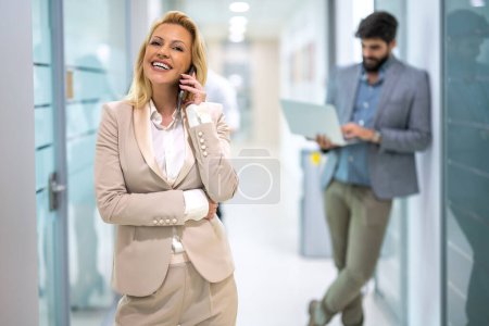 Téléchargez les photos : Portrait de jeune femme d'affaires blonde parlant sur téléphone portable dans le couloir du bureau. - en image libre de droit