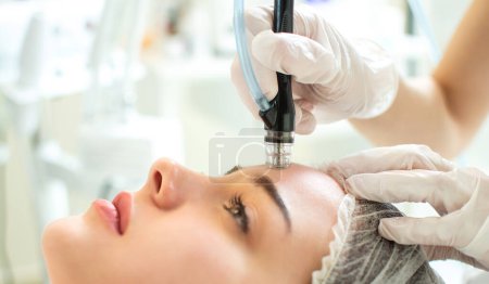 Téléchargez les photos : Gros plan de jeune femme recevant une thérapie de microdermabrasion sur le front au spa de beauté - en image libre de droit