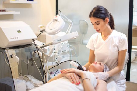 Téléchargez les photos : Médecin avec scraber à ultrasons faisant procédure de nettoyage par ultrasons du cou de la cliente au salon de beauté. - en image libre de droit