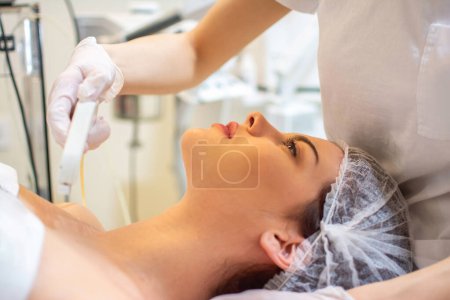 Téléchargez les photos : Esthéticienne appliquant un traitement avec un appareil moderne sur le cou de la jeune femme au salon de spa - en image libre de droit