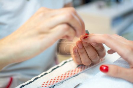 Photo for Closeup of a womans hand in a nail salon receiving a manicure by a beautician with nail file. - Royalty Free Image