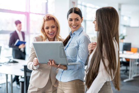 Beautiful multi-aged businesswomen standing in office hall, holding laptop and analyzing marketing data and companys growth, having consultation for business planning, strategy and financial budget.