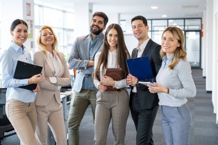 Groupe de jeunes gens d'affaires de la diversité en tenue formelle debout au bureau et regardant la caméra, posant et souriant