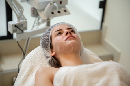 Téléchargez les photos : Headshot de belle femme portant un bonnet de protection allongé sur une table de massage au spa de luxe - en image libre de droit