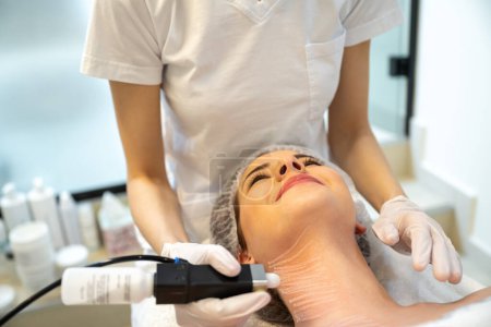 Photo for Closeup portrait of smiling female patient enjoying rejuvenation procedure performed by a beautician in a beauty clinic. - Royalty Free Image