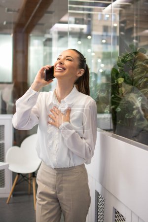 Foto de Agradable joven mujer de negocios hablando en el teléfono móvil en la oficina. - Imagen libre de derechos