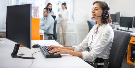 Téléchargez les photos : Portrait d'une travailleuse du service à la clientèle, opérateur souriant du centre d'appels avec casque téléphonique utilisant un ordinateur au bureau. - en image libre de droit