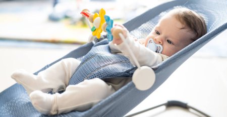 Téléchargez les photos : Adorable bébé garçon de 5 mois assis dans son fauteuil oscillant, jouant avec des jouets rotatifs. - en image libre de droit