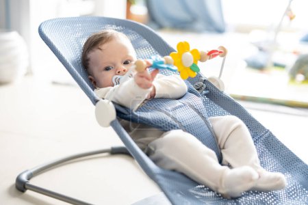 Téléchargez les photos : Adorable bébé garçon de 5 mois assis dans son fauteuil oscillant, jouant avec des jouets rotatifs. - en image libre de droit