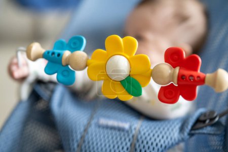 Foto de Primer plano de los juguetes de flores giratorias con el bebé acostado en el chait swing en el fondo. - Imagen libre de derechos