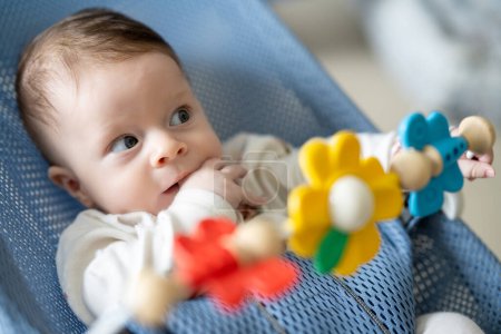 Téléchargez les photos : Adorable bébé garçon assis dans son fauteuil oscillant, jouant avec des jouets rotatifs. - en image libre de droit