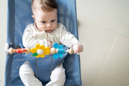 Téléchargez les photos : Adorable bébé garçon assis dans son fauteuil oscillant et jouant avec des jouets rotatifs. Vue grand angle. - en image libre de droit