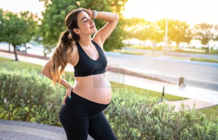 Foto de Hermosa mujer embarazada despreocupada en ropa deportiva disfrutando de la puesta del sol en el hermoso día de verano - Imagen libre de derechos