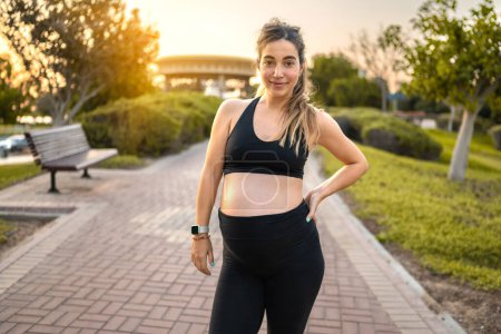 Téléchargez les photos : Portrait de jeune femme enceinte en tenue de sport dans le parc au coucher du soleil - en image libre de droit