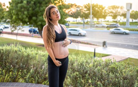 Foto de Encantadora mujer embarazada tocando su vientre al aire libre. Embarazo, embarazada, concepto de estilo de vida saludable - Imagen libre de derechos