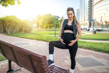Foto de Mujer embarazada joven en ropa deportiva en el parque al atardecer - Imagen libre de derechos