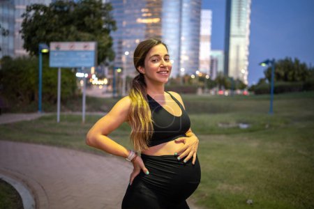 Photo for Portrait of smiling pregnant woman standing in the park at night. - Royalty Free Image