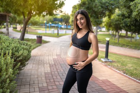 Foto de Retrato de una mujer embarazada de nueve meses mostrando su gran barriga en el parque al atardecer. - Imagen libre de derechos