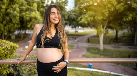 Retrato de una encantadora mujer embarazada apoyada en una valla de metal al aire libre. Embarazo, embarazada, concepto de estilo de vida saludable