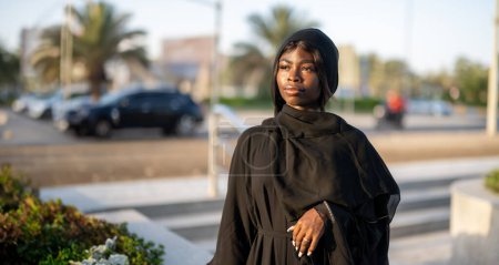 Téléchargez les photos : Portrait de belle femme musulmane portant la robe traditionnelle Abaya dans la rue de la ville au coucher du soleil - en image libre de droit