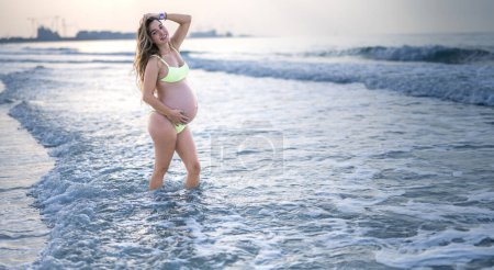 Photo for Beautiful pregnant woman in swimsuit posing on the beach at sunset - Royalty Free Image