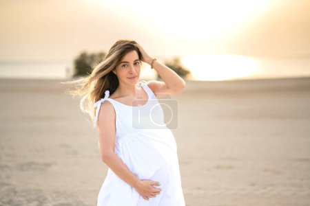 Téléchargez les photos : Portrait de belle femme enceinte en robe blanche sur la plage. - en image libre de droit